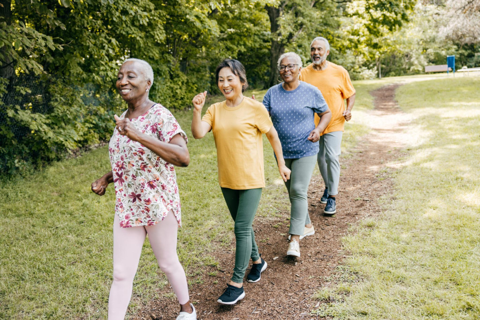 A group of smiling seniors walking together on a park trail